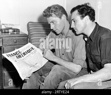 Hollywood, California:  1943 Actors Jean Pierre Aumont (L) and Gene Kelly (R) take break in the filming of the MGM movie, 'The Cross of Lorraine'. Kelly tought Aumont dance steps and Aumont returns the favor by teaching Kelly to speak French. Stock Photo
