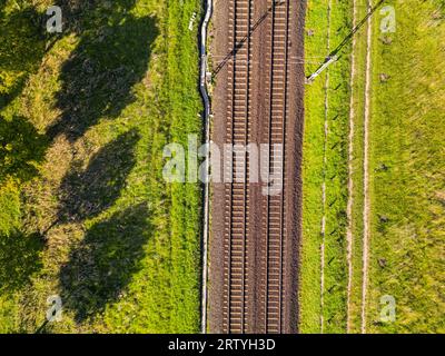 A railroad track with two lanes of tracks passes through nature directly from above as an aerial shot Stock Photo