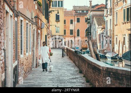 Woman walking her dog pet on the narrow cobblestone alleys along the water canals in Venice, Italy. Stock Photo