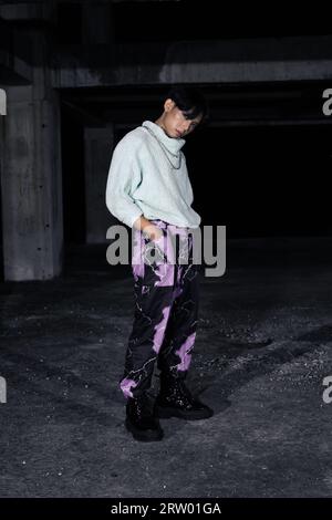 an asian man in black pants with a lightning pattern and a white sweater stands in a haunted building Stock Photo