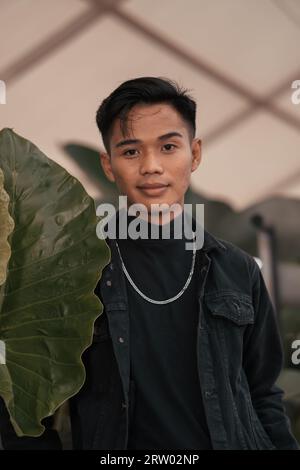 an asian boy in a black denim jacket posing like a naughty boy with a chain around his neck in a park in the afternoon Stock Photo