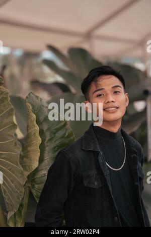 an asian boy in a black denim jacket posing like a naughty boy with a chain around his neck in a park in the afternoon Stock Photo