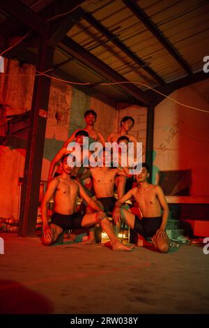 a group of men without clothes dancing poses in an old building with a red light at night Stock Photo