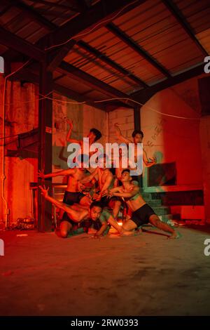 a group of men without clothes dancing poses in an old building with a red light at night Stock Photo