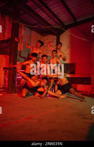 a group of men without clothes dancing poses in an old building with a red light at night Stock Photo