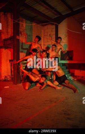 a group of men without clothes dancing poses in an old building with a red light at night Stock Photo