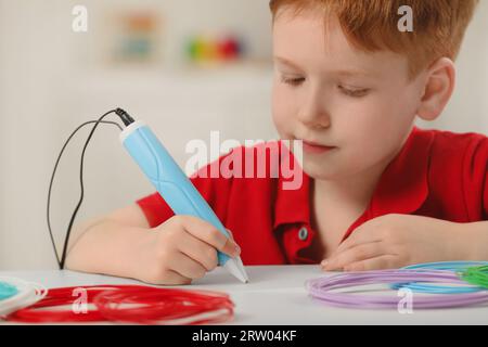 Boy drawing with stylish 3D pen at white table Stock Photo