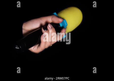 Female person hand close-up holding microphone professional karaoke singing equipment on black background. Stock Photo