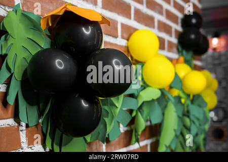 Bright objects, decorations on a brick wall, indoors, interior in the style of a Hawaiian party, tropics, jungle and black air helium balloons. Stock Photo