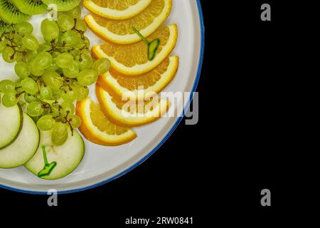 Fruit plate with grapes, kiwi, lime, pear and orange, sliced pieces on a black background, isolated. Stock Photo