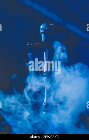 Hookah head, clay bowl and pipe, smoking object in smoke and blue light, relaxation atmosphere. Stock Photo