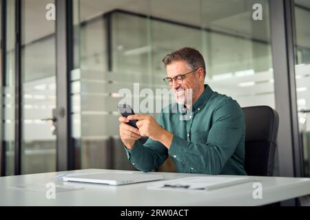 Smiling mid aged business man using cell phone at work desk. Stock Photo