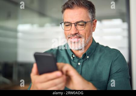 Busy smiling business man looking at phone working on mobile in office. Stock Photo