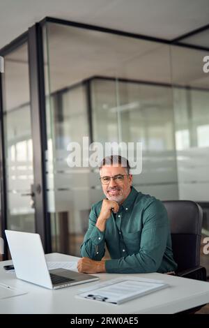 Middle aged business man sitting at work desk in office, vertical portrait. Stock Photo