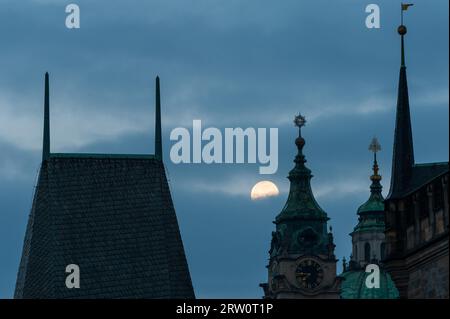 Bridge tower of Charles bridge in Prague over the Vlatva river at night with full moon in sky behind clouds Stock Photo