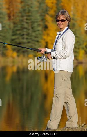 Woman fishing at a lake reflecting the beautiful colored trees in Chena River State Recreation Area Stock Photo