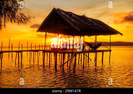 Native people relaxing in hammocks on wooden jetty during sunset on Kri island, Raja Ampat, West Papua, Indonesia Stock Photo
