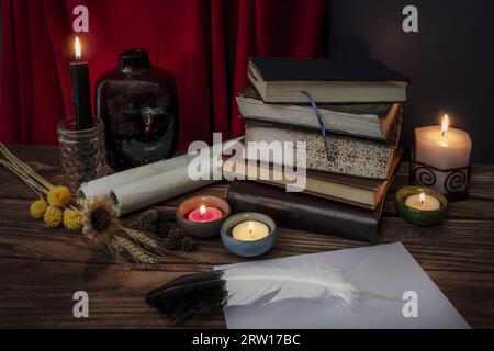 A still life with some dried flowers, some lit candles and a block of old books along with a pen on a sheet of paper Stock Photo