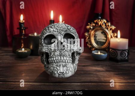A Gothic-style still life with a decorated skull, lit candles and a crimson red cloth Stock Photo