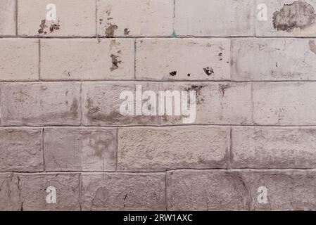A stone block wall painted with cream-colored paint with many obvious chips Stock Photo