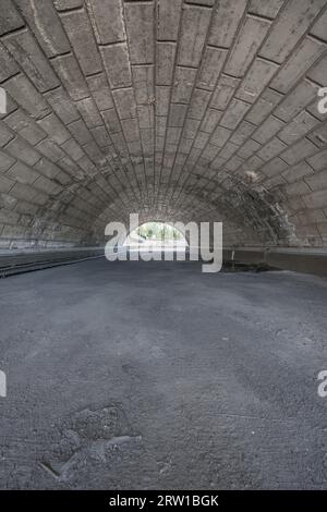 A concrete and stone tunnel under a highway Stock Photo