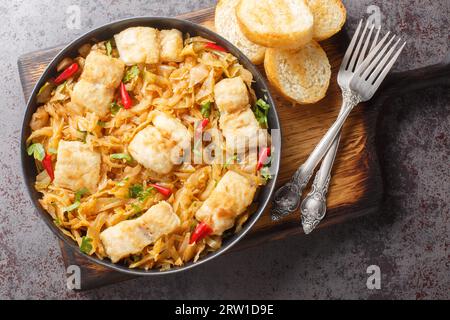 Stewed white cabbage with sea fish fillet, onion and chili pepper close-up in a plate served with toast on the table. horizontal top view from above Stock Photo