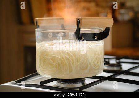 Udon noodle boiling in glass saucepan on gas stove Stock Photo