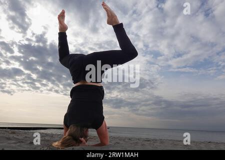 07.09.2022, Germany, Mecklenburg-Western Pomerania, Wustrow - Woman doing a headstand while doing yoga on the beach. 00S220907D084CAROEX.JPG [MODEL RE Stock Photo