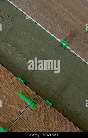 Tile levelling system, four plastic green clips with wedges. Close-up view, selective focus, blurred background. Stock Photo