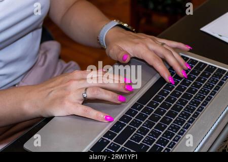 Close up female hands with pink nail manicure typing on laptop keyboard. Stock Photo