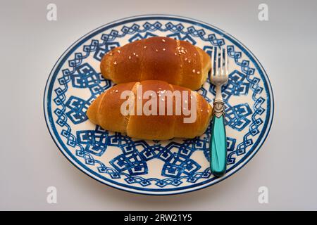 Two pieces of salt bread and one fork on a white plate with a blue pattern Stock Photo