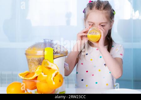 Adorable girl tasting freshly made orange juice at kitchen Stock Photo