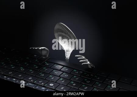Spoon and fork in the form of a man working at a computer keyboard. Stock Photo