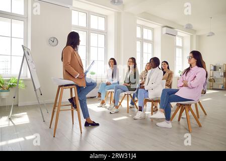 Young woman coach gives presentation for diverse women at professional business training meeting Stock Photo