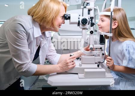 Smiling oculist checking little girl eyesight on modern optical equipment Stock Photo