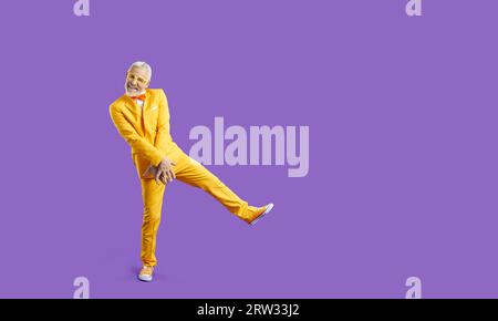 Cheerful eccentric and funny senior man in bright stylish clothes isolated on purple background. Stock Photo