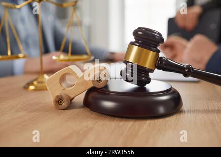 Toy car, sound block, gavel and scales of justice on table, with accident lawyers in background Stock Photo