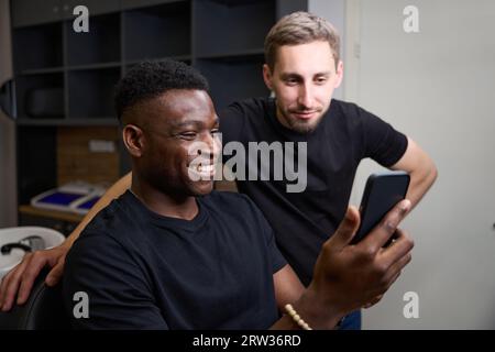 Smiling African American guy communicates online on phone in barbershop Stock Photo