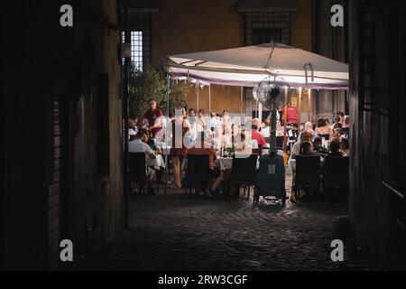 Rome, Italy - August 27, 2023: Roman nightlife with patrons enjoy soclialising and dining at an outdoor restaurant on a late summer night in the histo Stock Photo