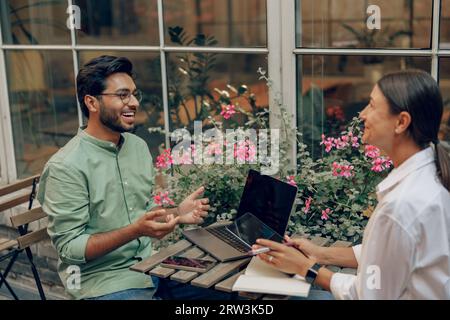Smiling business colleagues discuss biz issue while use laptop sitting in office terrace Stock Photo