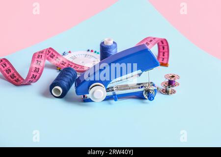 Manual sewing machine with measuring tape and thread spools on color background Stock Photo