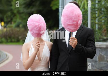Bride and groom covering their faces with cotton candies outdoors Stock Photo