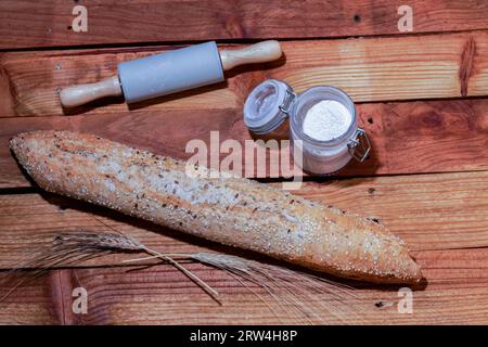 Loaf of rustic artisan bread with different types of seeds, wheat ears, flour and rolling pin on a wooden table Stock Photo