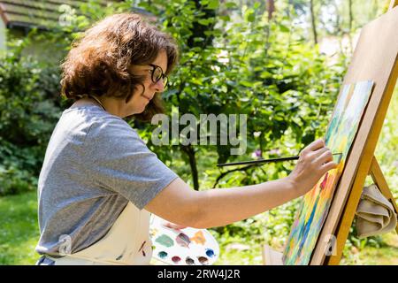 Woman painting at a canvas with paint brush, woman painting at a canvas with paint brush Stock Photo