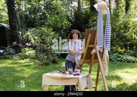 Frau malt ein Bild im Garten, Frau malt ein Bild in einem Garten Stock Photo