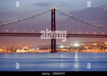 25th of April (Portuguese: Ponte 25 de Abril) Bridge over Tagus river at night and city of Lisbon, Portugal in the background Stock Photo
