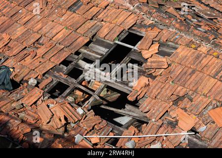 Hole in damaged clay tiled roof with wooden frame of a traditional building Stock Photo