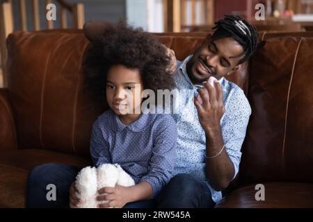 Smiling caring African American father combing little daughter hair Stock Photo