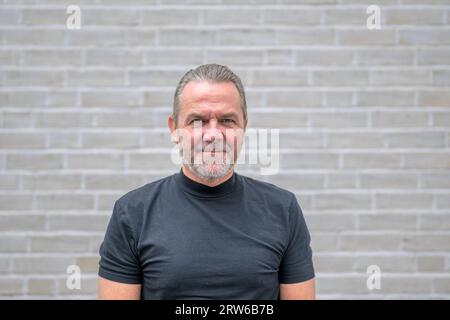 Portrait of an attractive serious man looking to camera in front of a white brick wall Stock Photo
