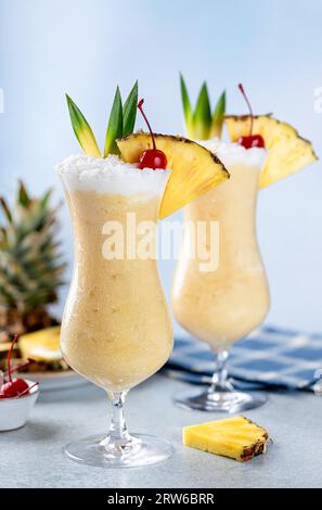 Pina colada cocktails with cherry, pineapple slice and leaves on a blue background Stock Photo